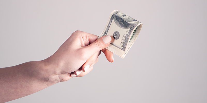 A hand holding a couple of hundred dollar bills