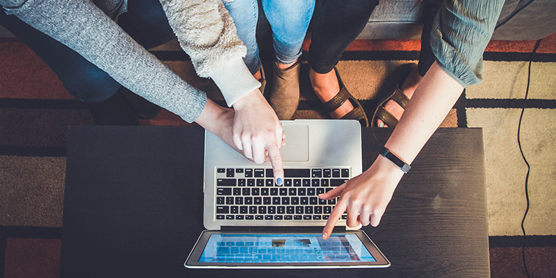 Three pair of hands pointing to a laptop screen