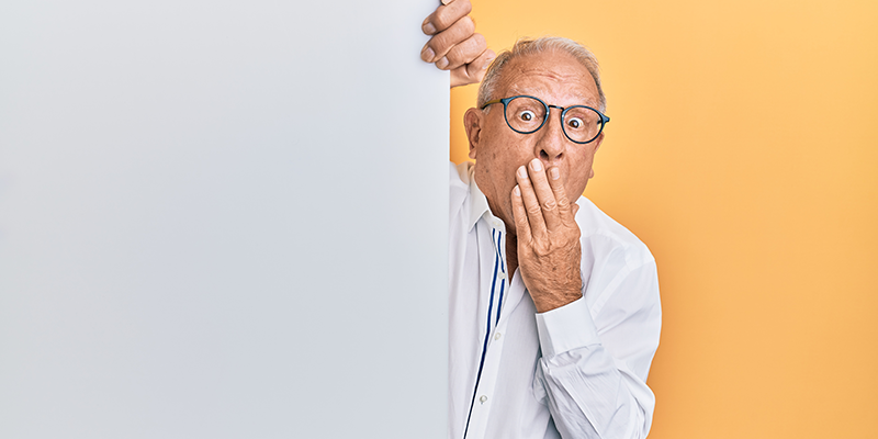 Senior caucasian man holding blank empty banner covering mouth with hand